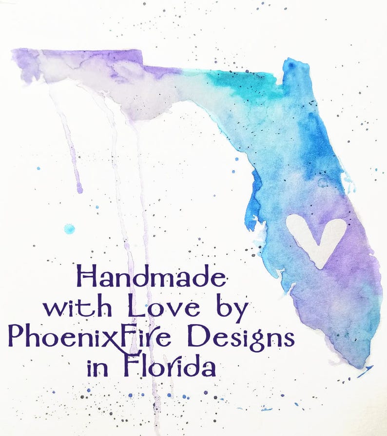 May include: A watercolour painting of the state of Florida with a white heart in the centre. The painting is in shades of blue and purple with white splatters. The text "Handmade with Love by PhoenixFire Designs in Florida" is written below the painting.