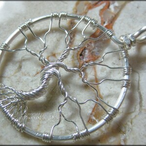 May include: A silver wire wrapped tree of life pendant with a circular design. The pendant is on a white background.