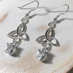 May include: Silver earrings featuring a Celtic knot design and a clear crystal drop. The earrings are silver in colour and have a delicate design.