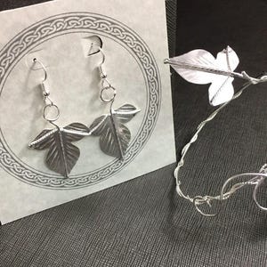 May include: Silver leaf earrings and a matching silver leaf bracelet. The earrings are dangle earrings with two leaves on each earring. The bracelet is a delicate wire bracelet with a single leaf charm.