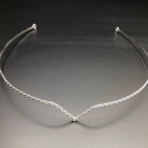 May include: A silver braided headband with a v-shaped design.