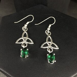 May include: Silver Celtic knot earrings with green gemstone drops. The earrings have a traditional Celtic knot design and feature a dangling green gemstone.