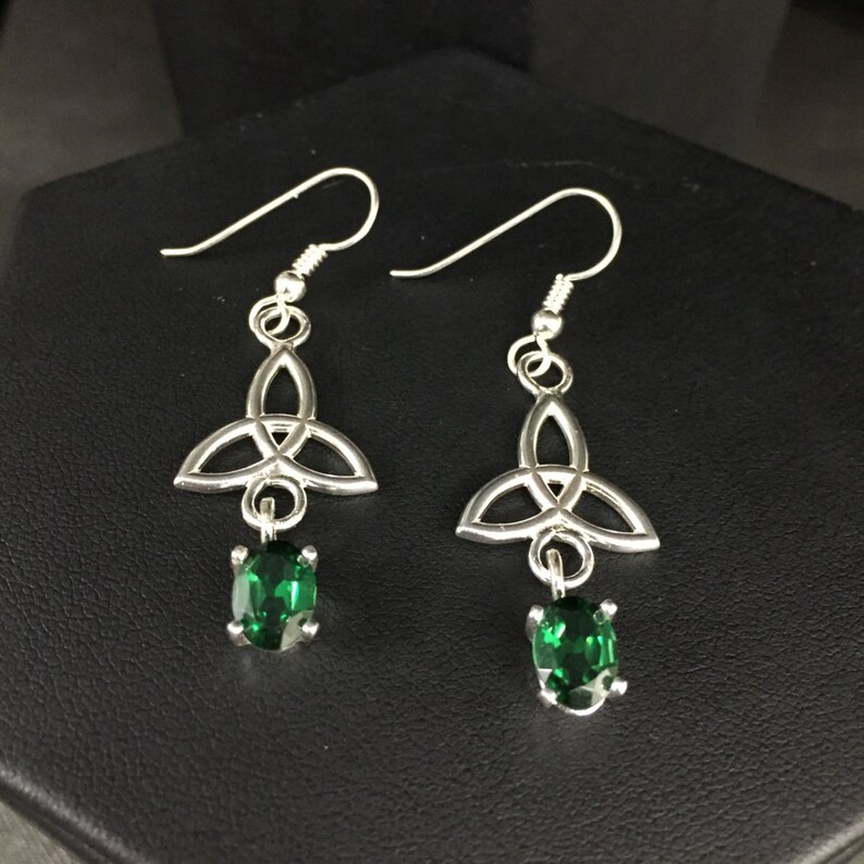 May include: Silver Celtic knot earrings with green gemstone drops. The earrings have a traditional Celtic knot design and feature a dangling green gemstone.
