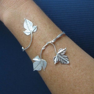 May include: Silver bracelet with a vine design featuring three leaves. The bracelet is open and adjustable.