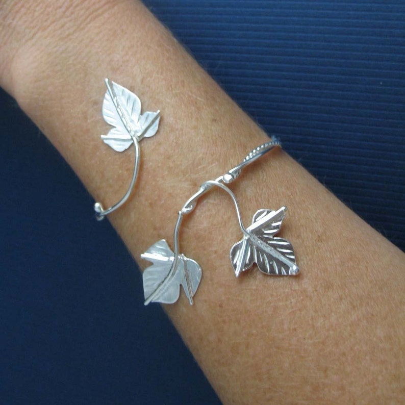 May include: Silver bracelet with a vine design featuring three leaves. The bracelet is open and adjustable.