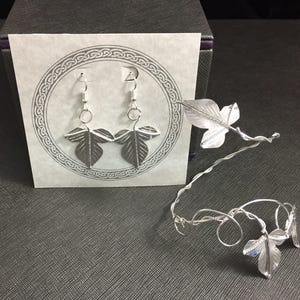 May include: A pair of silver earrings with leaf designs and a silver leaf headband.
