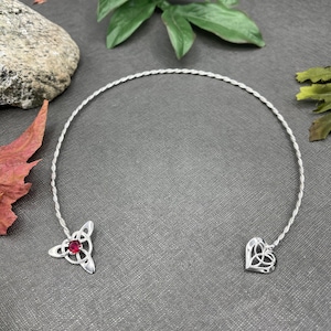 May include: Silver Celtic knot headband with a red gemstone. The headband is twisted and has a heart and a trinity knot design.