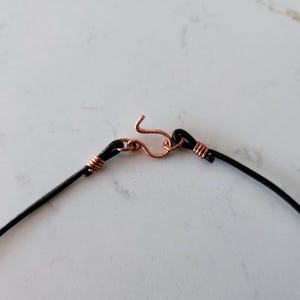 May include: A black leather cord necklace with a copper clasp.