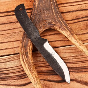 May include: A black knife with a wooden handle and a white blade. The knife is lying on a wooden surface with a piece of antler.