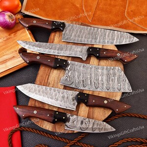 May include: Set of five kitchen knives with wooden handles and Damascus steel blades. The knives are arranged on a wooden cutting board with a brown leather background.
