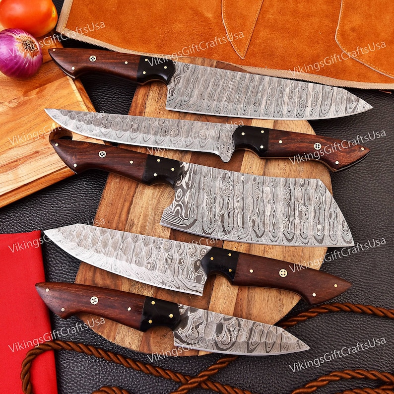 May include: Set of five kitchen knives with wooden handles and Damascus steel blades. The knives are arranged on a wooden cutting board with a brown leather background.