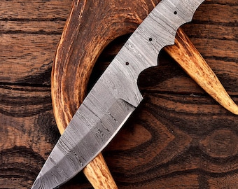 Peut inclure: Gros plan sur une lame de couteau argentée avec une finition à motifs. La lame repose sur une pièce de bois de cerf.