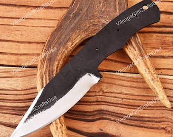 May include: A black knife with a silver blade, resting on a piece of antler. The knife is on a wooden surface.