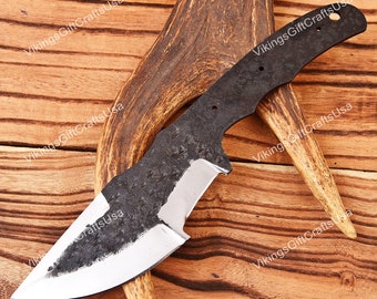 May include: A forged steel knife blade with a textured, dark finish and a polished, silver-colored cutting edge. The blade is displayed on a wooden surface with a deer antler.
