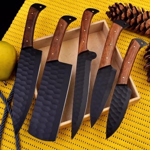 May include: Set of five black kitchen knives with wooden handles. The knives have a hammered finish and are displayed in a wooden box.
