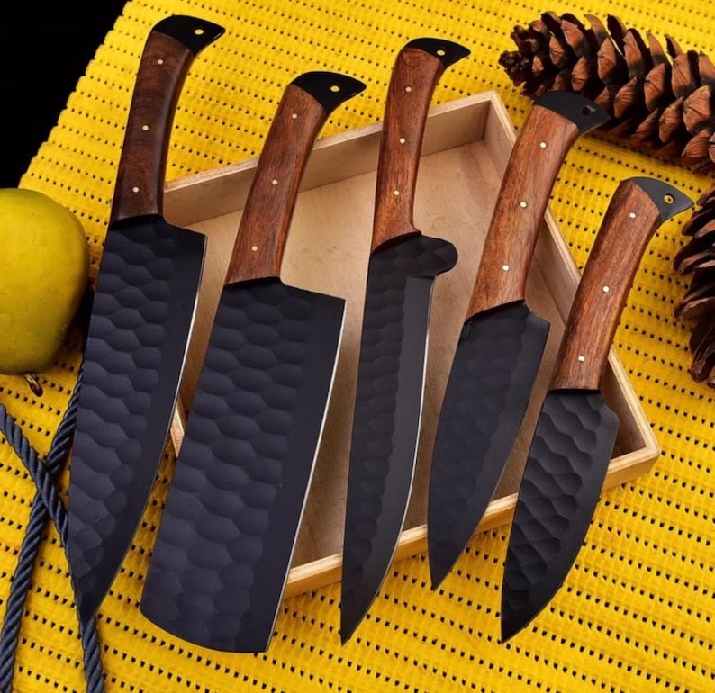 May include: Set of five black kitchen knives with wooden handles. The knives have a hammered finish and are displayed in a wooden box.