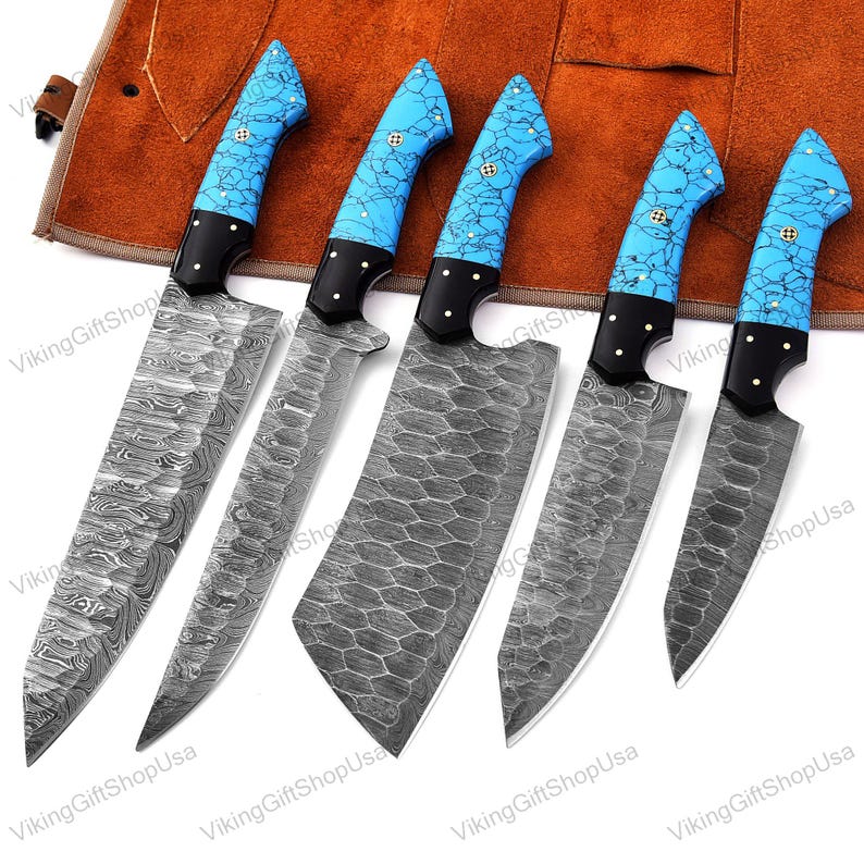 May include: Set of five kitchen knives with blue and white patterned handles. The knives have a Damascus steel blade and are displayed on a brown leather roll.