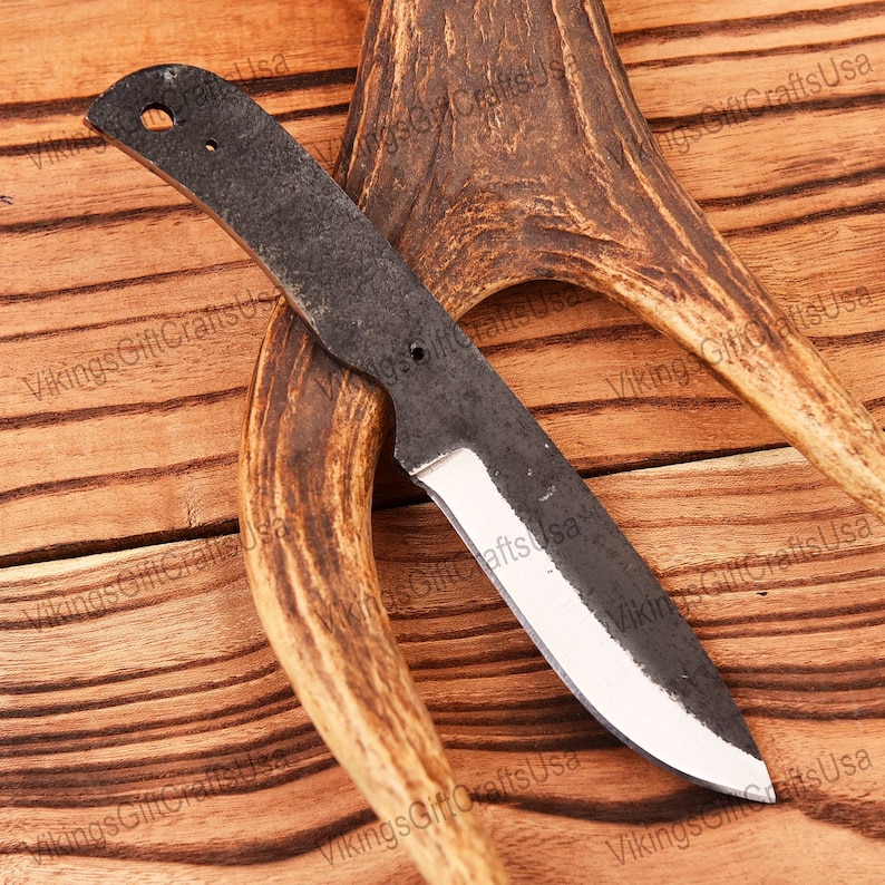 May include: A hand-forged knife with a black blade and a wooden handle. The knife is resting on a piece of antler.