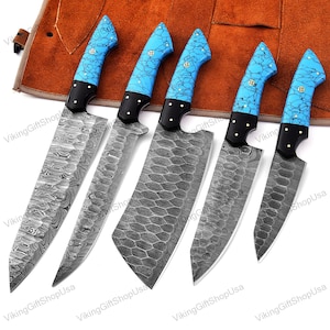 May include: Set of five kitchen knives with blue and white patterned handles. The knives have a Damascus steel blade and are displayed on a brown leather roll.