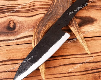 May include: A black, forged steel knife blade with a sharp, silver edge. The knife is set against a wooden background with a deer antler. The blade has a rustic, textured finish.