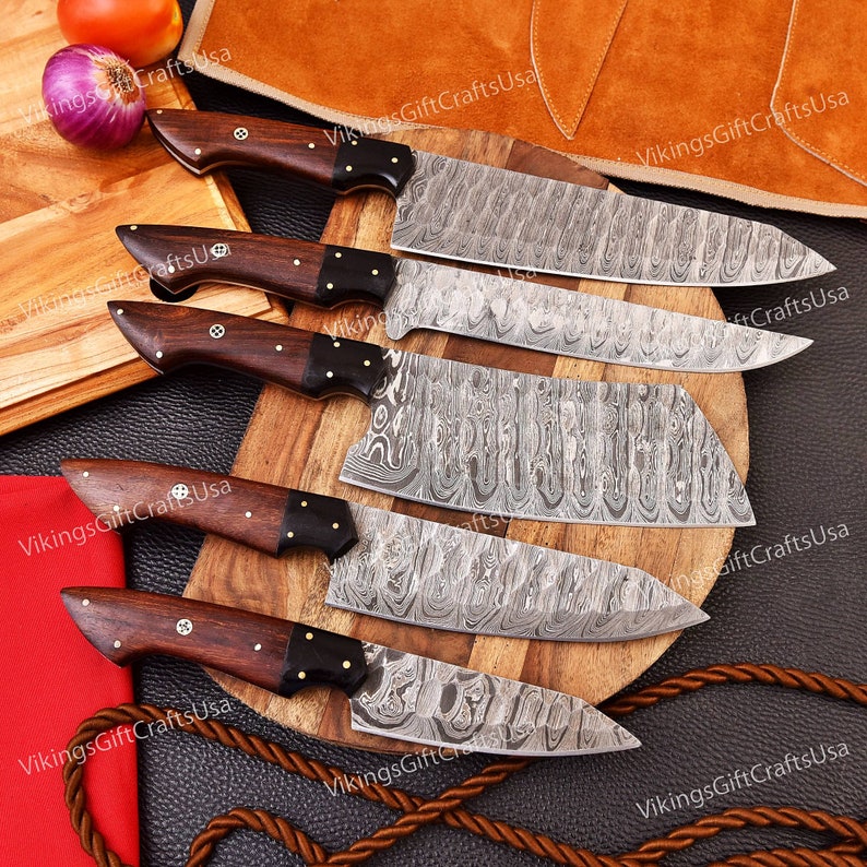 May include: Set of six kitchen knives with wooden handles and Damascus steel blades. The knives are arranged on a wooden cutting board and a brown leather surface.
