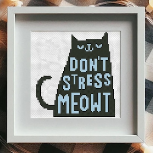 Könnte beinhalten: Ein gerahmtes Kreuzstich-Kunstwerk mit einer schwarzen Katzen-Silhouette und dem Text "DON'T STRESS MEOWT" in Blau und Schwarz. Das Kunstwerk befindet sich in einem weißen Rahmen, umgeben von einer Lichterkette mit warmweißen Lichtern, auf kariertem Hintergrund.