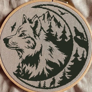 May include: Black and white embroidery of a wolf's head with a crescent moon and forest behind it. The embroidery is in a wooden hoop.