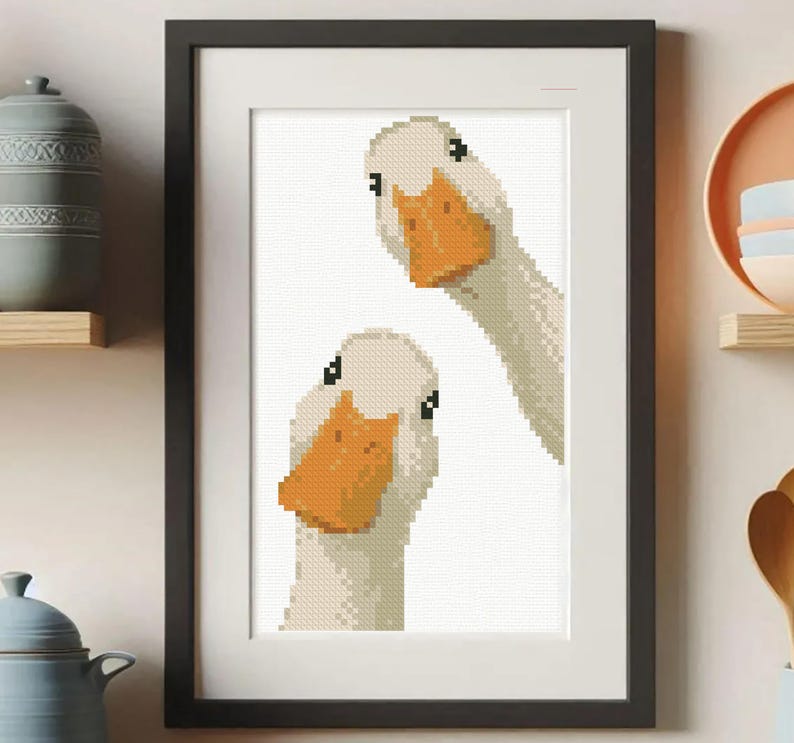 May include: Framed art print featuring a pixelated illustration of two white geese with orange beaks and black eyes. The artwork is set against a white background and framed in a black frame. The print is a whimsical addition to any home decor.