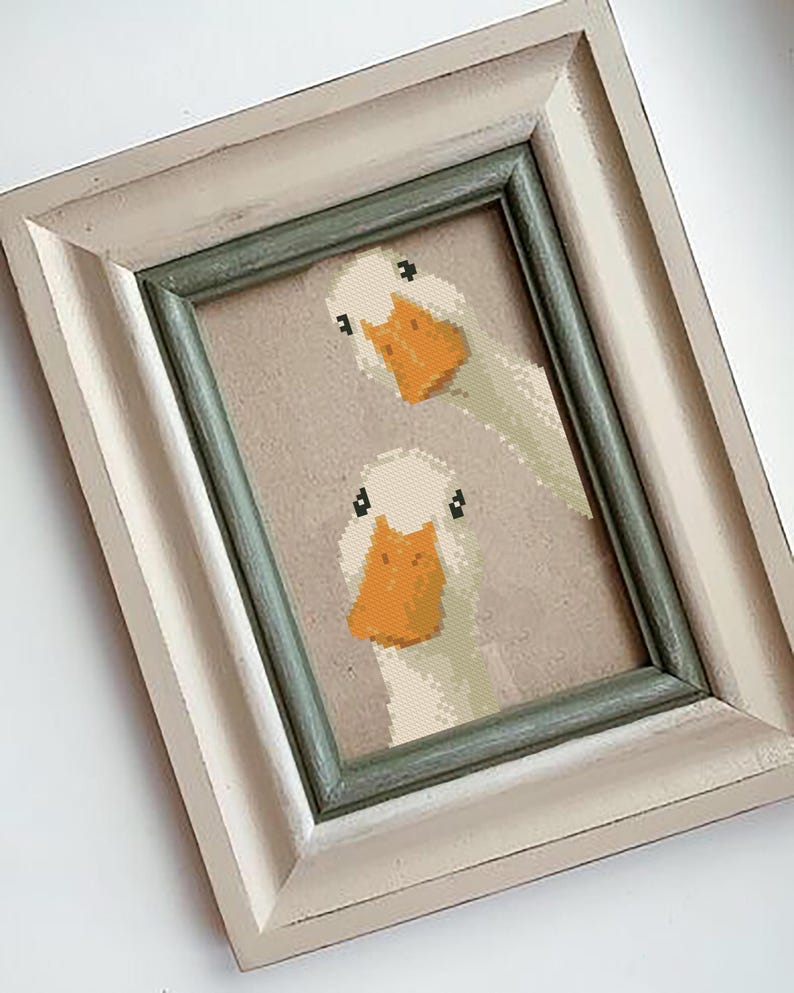 May include: Framed cross-stitch art featuring two white geese with orange beaks and black eyes. The artwork is set against a neutral background and framed in a distressed white and green frame. A charming piece of home decor.
