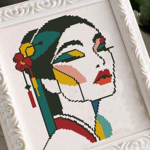 Puede incluir: Un patrón de punto de cruz colorido de la cara de una mujer con formas geométricas y una flor en el pelo.