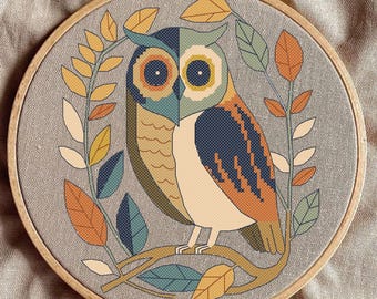 May include: A cross-stitch embroidery hoop with a colorful owl design. The owl is perched on a branch with leaves in shades of green, orange, and yellow. The background is a light gray fabric.