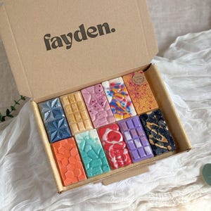 May include: A cardboard box with the text fayden printed on the inside lid, containing ten rectangular wax melts in various colors and textures. The collection includes geometric, honeycomb, and marbled patterns in blue, gold, pink, orange, and black.