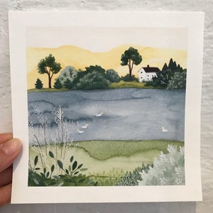 May include: A watercolor painting of a white house with a brown roof on a hill overlooking a lake. The lake is a light blue color and there are a few white birds flying over it. The sky is a light yellow color and there are green trees and bushes in the foreground.