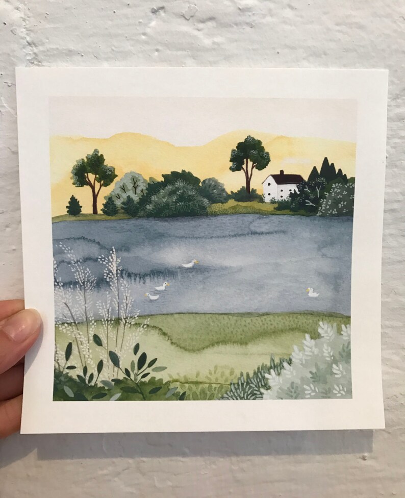 May include: A watercolor painting of a white house with a brown roof on a hill overlooking a lake. The lake is a light blue color and there are a few white birds flying over it. The sky is a light yellow color and there are green trees and bushes in the foreground.