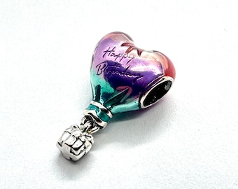 Op de afbeelding: Een hartvormige bedel met een verloop van roze, paars en teal, met de tekst "Happy Birthday". De bedel is bevestigd aan een zilverkleurige cadeau-doos hanger. Dit sieraad is ontworpen voor een verjaardagsviering.