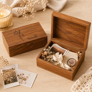 May include: Two rectangular wooden boxes with a dark brown grain finish. One box is closed and features a laser-engraved floral design and the name Sarah. The other box is open, containing dried flowers, a ribbon, a small photograph, and a note.