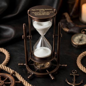 May include: A bronze-toned metal hourglass with white sand, featuring a ship's wheel base and an integrated compass. The top plate is engraved with: Happy 25th Wedding Anniversary My Love - Like sands of time our love grows deeper each day. Forever yours, together always, hand in hand, heart to heart.