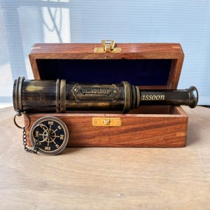 Peut inclure: Une longue-vue en laiton avec une finition sombre et patinée, portant l'inscription gravée DOLLOND LONDON et le mot assoon. Elle repose dans une boîte en bois à doublure bleue, accompagnée d'une petite boussole circulaire en laiton sur chaînette.