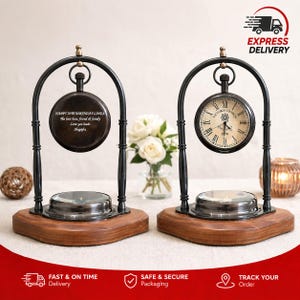 May include: Two black metal arched stands on wooden bases, each holding a circular object. The left object is a dark disc engraved with "HAPPY 70TH BIRTHDAY LINDA The best boss, friend & family Love you loads Shagufta". The right is a clock face.