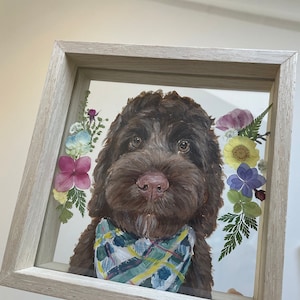 Könnte beinhalten: Ein gerahmtes Kunstwerk aus gepressten Blumen mit einem braunen Hund mit einem blau-grünen Halstuch. Der Hund ist umgeben von gepressten Blumen in den Farben Rosa, Lila, Gelb und Grün.