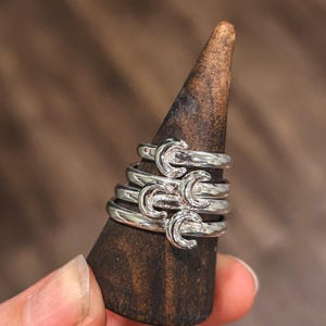 May include: A silver ring with a wavy design. The ring is stacked on a wooden ring holder.