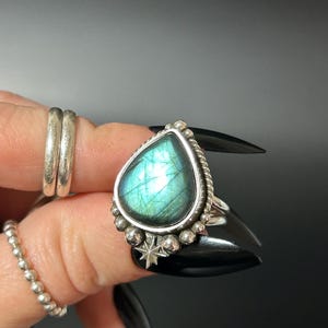 May include: A silver ring with a teardrop-shaped blue labradorite gemstone and a starburst design.