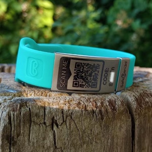 Könnte beinhalten: Ein türkisfarbenes Silikonarmband mit einer silbernen Metallplatte, auf der "SCAN ME" steht und ein QR-Code abgebildet ist. Das Armband trägt außerdem die Aufschrift "CODE: Safe&Sound".