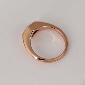 May include: Rose gold ring with a rectangular face and a smooth, polished band. The ring has a modern, minimalist design and a warm, metallic hue. The ring is a size 7.
