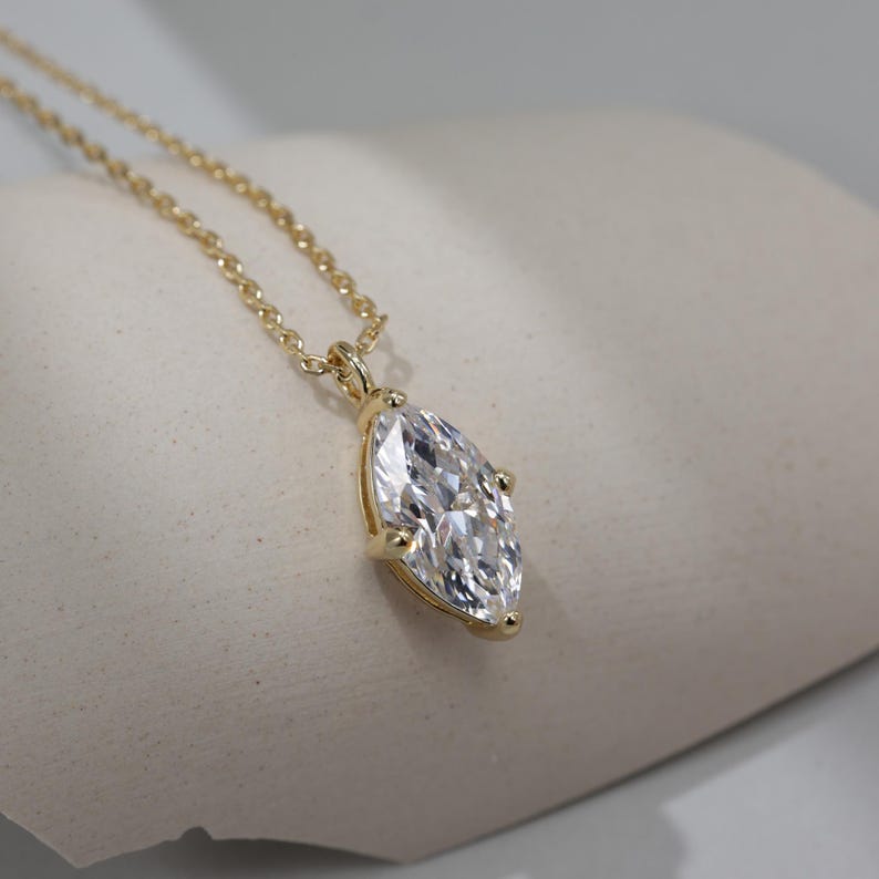 May include: A gold chain necklace with a large, clear marquise-shaped pendant.