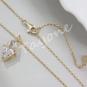 May include: A gold chain necklace with a large, clear, pear-shaped gemstone pendant. The chain has an adjustable length.