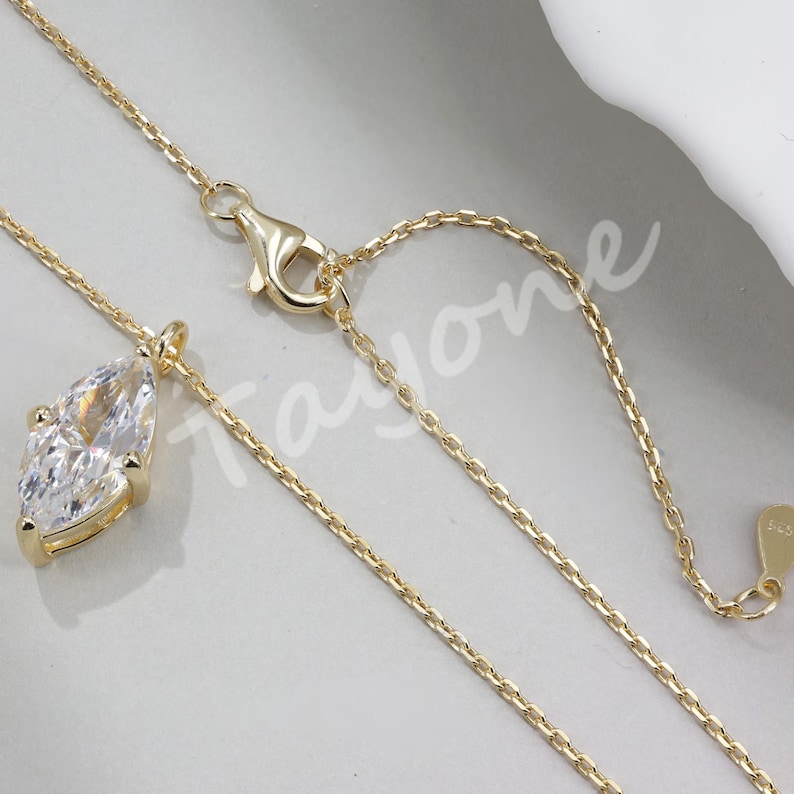 May include: A gold chain necklace with a large, clear, pear-shaped gemstone pendant. The chain has an adjustable length.