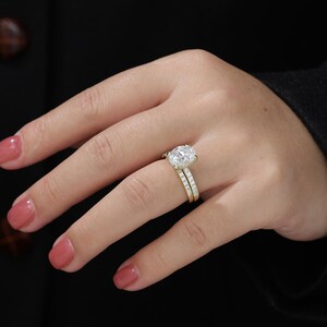 Op de afbeelding: Een close-up van een vrouwenhand met een gouden verlovingsring met een grote ovale diamant en een bijpassende trouwring.
