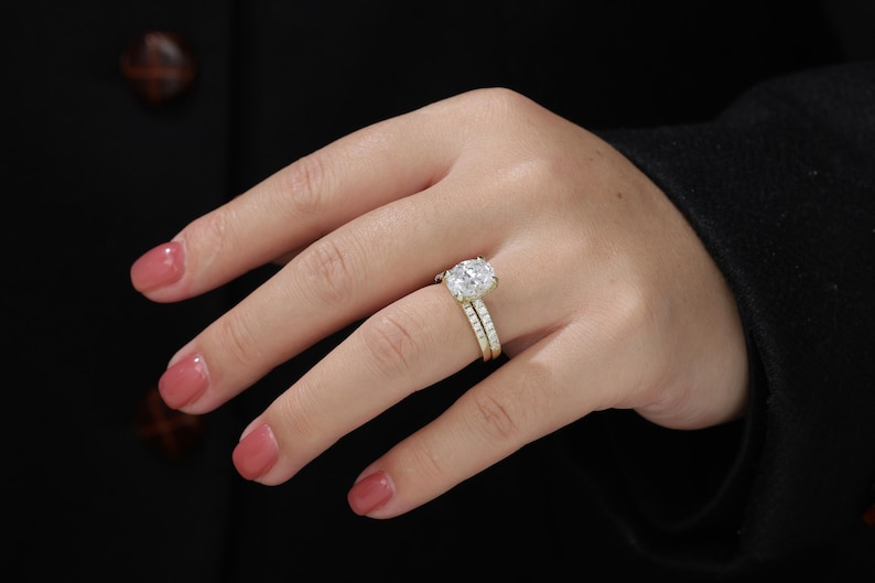 Op de afbeelding: Een close-up van een vrouwenhand met een gouden verlovingsring met een grote ovale diamant en een bijpassende trouwring.