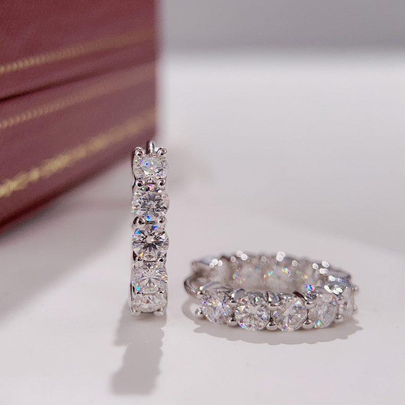 Puede incluir: Un par de pendientes de aro de plata con una fila de piedras redondas transparentes brillantes.